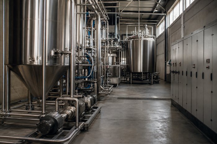 Sala de proceso cervecero con tanques de acero inoxidable, tubería sanitaria y tableros eléctricos.